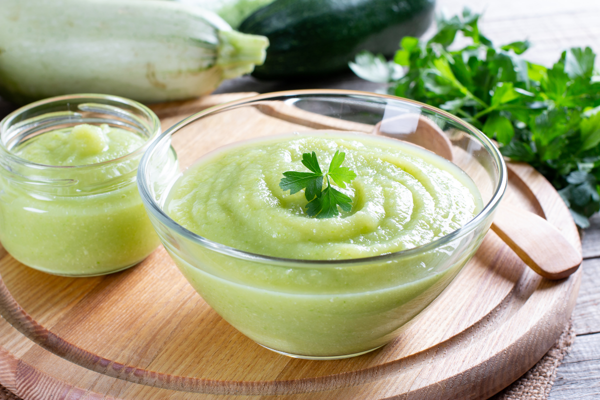 Zucchini puree in a glass jar with fresh zucchini on the background.